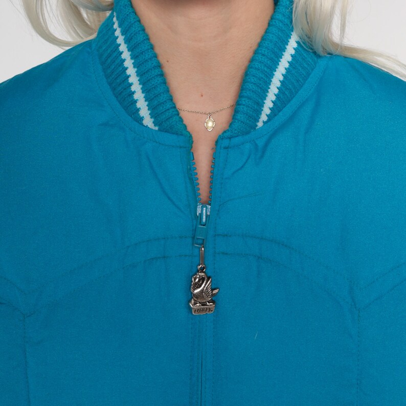 May include: A teal blue bomber jacket with a white and teal striped collar and a zipper with a swan charm.
