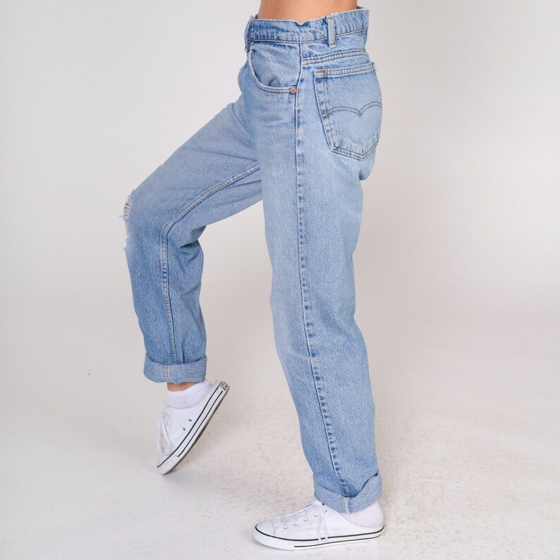 May include: A pair of light blue denim jeans with a cuffed hem. The jeans have a relaxed fit and are worn with white trainers.