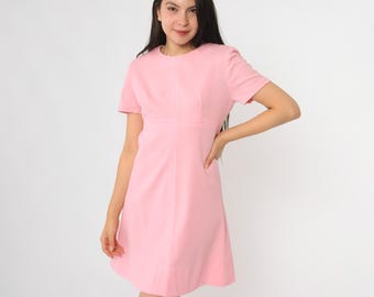 May include: A light pink, short-sleeved dress with a round neckline. The dress has a fitted bodice and a flared skirt. The model is wearing the dress. The dress is made of a smooth, solid-colored fabric.