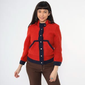 May include: A red and navy blue jacket with a zipper closure and button accents. The jacket has a textured, fuzzy fabric.