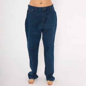 May include: Dark blue denim jeans with a classic five-pocket design. The jeans have a straight leg cut and a button and zipper closure. The denim appears to be a medium weight, suitable for everyday wear.