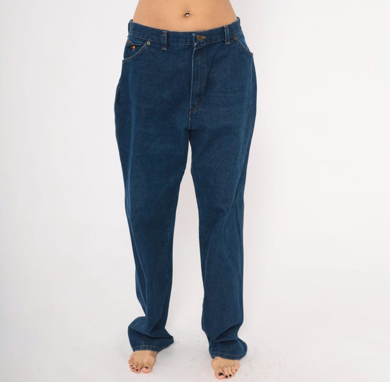 May include: Dark blue denim jeans with a classic five-pocket design. The jeans have a straight leg cut and a button and zipper closure. The denim appears to be a medium weight, suitable for everyday wear.