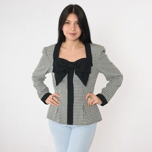 May include: A black and white gingham blazer with a large black bow at the neckline. The blazer has a fitted silhouette and long sleeves.