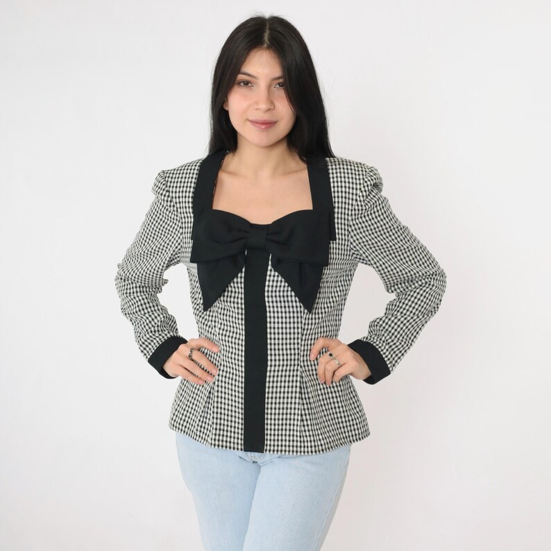 May include: A black and white gingham blazer with a large black bow at the neckline. The blazer has a fitted silhouette and long sleeves.