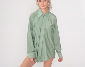 May include: A long-sleeved shirt in a pale green hue. The shirt features a classic collar, a chest pocket, and buttoned cuffs. The fabric looks lightweight. The shirt is unbuttoned and worn as a top. The shirt is a versatile piece of clothing.