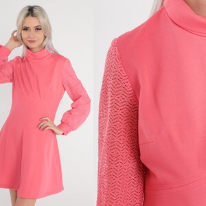 May include: A pink dress with a high neck and long sleeves. The sleeves are made of a lacy material. The dress has a fitted bodice and a flared skirt.
