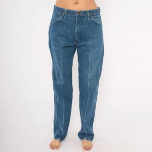 Puede incluir: Vaqueros azules de mezclilla con un dise&ntilde;o cl&aacute;sico de cinco bolsillos. Los vaqueros tienen un corte de pierna recta y cierre de bot&oacute;n y cremallera. La mezclilla es de lavado medio y los vaqueros parecen vintage.
