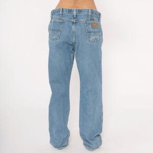 Peut inclure: Jean bleu clair avec une coupe classique &agrave; cinq poches. Le jean pr&eacute;sente une coupe droite et un patch en cuir marron sur la poche arri&egrave;re avec le nom de la marque. Le jean est en denim durable.