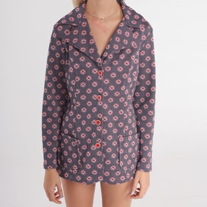 Puede incluir: Una chaqueta azul con estampado floral rosa y botones rojos. La chaqueta tiene cuello y mangas largas.