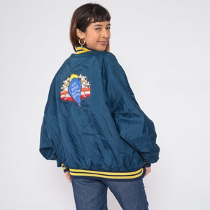 May include: A dark blue bomber jacket with a yellow and navy blue striped trim. The back of the jacket features an embroidered patch of a hot air balloon with the text "Cool, Pete's Balloon Place".