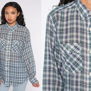 Op de afbeelding: Een geruit shirt met lange mouwen in tinten blauw, groen en wit. Het shirt heeft een knoopsluiting, een kraag en twee borstzakken. Het ruitpatroon is een klassiek ontwerp.