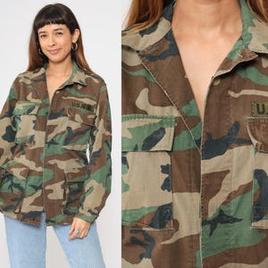 May include: A green, brown, and black camouflage jacket with a button closure and two flap pockets. The jacket has a patch on the right side that says "U.S. ARMY".
