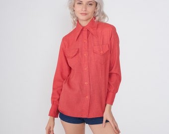 Puede incluir: Una camisa de manga larga de color rojo con cuello de punta y dos bolsillos de solapa. La camisa tiene cierre de botones en la parte delantera y está hecha de una tela suave y texturizada.