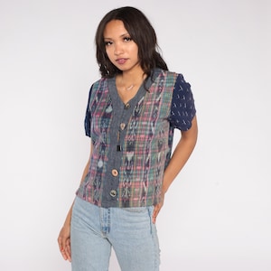 May include: A button-down shirt with a V-neckline. The shirt features a colorful plaid pattern in pink, green, and blue, with denim accents and short navy sleeves. The shirt is paired with light blue jeans.