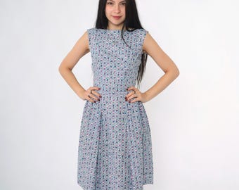 May include: A sleeveless, light blue dress with a floral pattern. The dress features a fitted bodice and a flared skirt, with a round neckline. The floral pattern includes pink, green, and blue elements. The dress is knee-length.