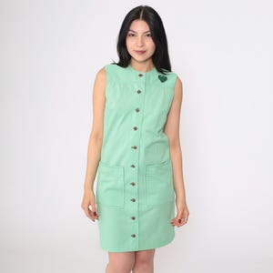 Pode incluir: Um vestido sem mangas de cor verde menta com fecho de botões na frente e dois bolsos de remendo. O vestido tem um design simples e clássico.