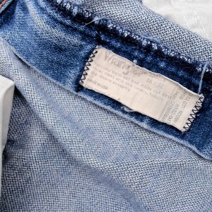 May include: Close-up of blue denim jeans, showing the inside pocket and the Wrangler label. The jeans have a classic, worn look with visible stitching and a metal button. The label provides size and care instructions.