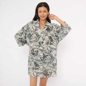 Può includere: Una camicia abbottonata con un motivo monocromatico di foglie tropicali grigie e bianche. Il capo ha una vestibilità rilassata, un colletto classico e maniche lunghe arrotolate. Il tessuto presenta una fitta stampa botanica all-over.
