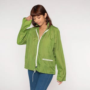 May include: A lime green windbreaker jacket with a white zipper and drawstring. The jacket has a high collar and a small pocket with a white zipper. The jacket is lightweight and appears to be made of nylon or a similar material.