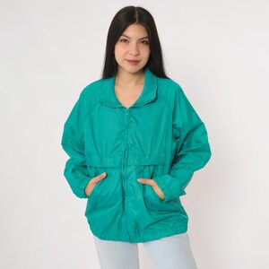 May include: Teal-colored windbreaker jacket with a full zipper closure, two front pockets, and a stand-up collar. The jacket is made of a lightweight, possibly nylon, material. The jacket is a solid color and has a relaxed fit.
