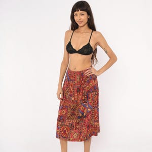 May include: A black lace bralette with thin straps and a midi-length skirt featuring a vibrant, multi-colored patchwork pattern in shades of red, orange, yellow, and blue. The skirt has an elasticized waistband and a loose, flowing silhouette.