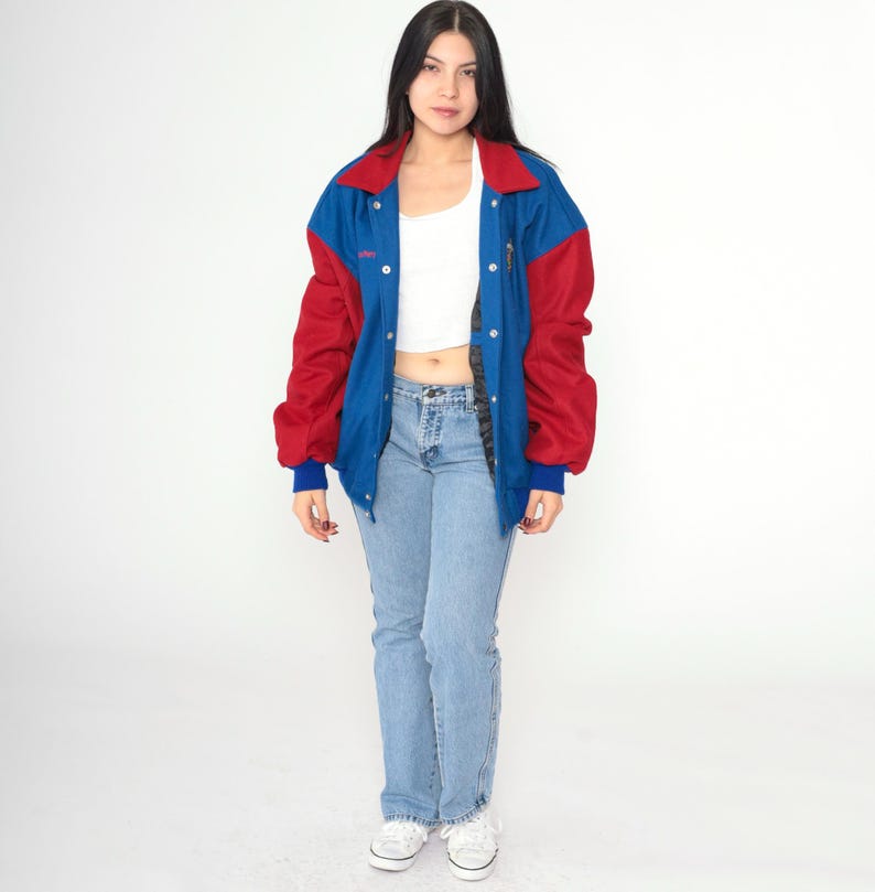 May include: A blue and red varsity jacket with a snap closure. The jacket has a white collar and a white stripe down the sleeves.