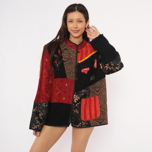 May include: A long-sleeve jacket featuring a patchwork design with various fabric textures and patterns in shades of red, black, and brown. The jacket includes a mandarin collar, toggle closures, and a prominent red rectangular pocket on the front.