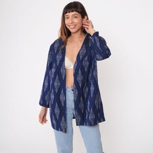 May include: A navy blue open-front jacket with a diamond pattern in shades of blue and beige. The jacket has long sleeves and a relaxed fit, suitable for layering. The model is wearing light blue jeans.
