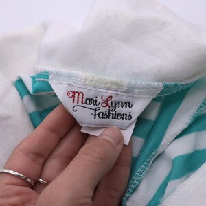 May include: Close-up of a white and turquoise striped shirt with a white tag that reads "Mari Lynn Fashions".