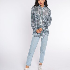 Op de afbeelding: Een geruit overhemd in groen, blauw en wit, gecombineerd met lichtblauwe jeans en witte hoge sneakers. Het overhemd heeft twee borstzakken en lange mouwen. Het model staat voor een witte achtergrond.