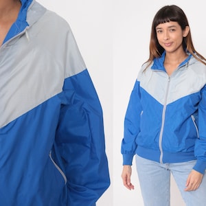 May include: A blue and silver windbreaker jacket with a zipper closure and a hood. The jacket has a color block design with a silver top and a blue bottom.