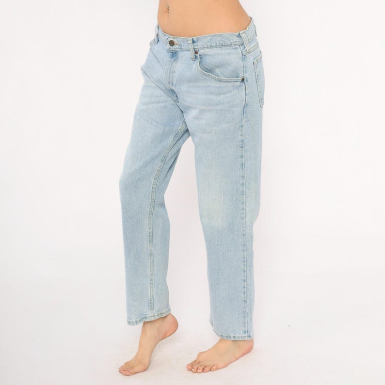 May include: Light blue denim jeans. The jeans have a classic five-pocket design, a button and zipper closure, and a straight leg fit. The jeans are a light wash, with subtle fading and wear.