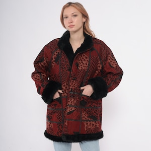 May include: A red and black patterned coat with black fur trim on the collar, cuffs, and hem. The coat features a patchwork design with animal print patterns and a button closure. The coat has pockets.