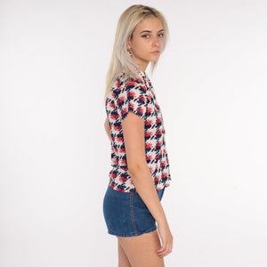 May include: A white button-up shirt with a red and blue geometric pattern. The shirt has short sleeves and a collared neckline.