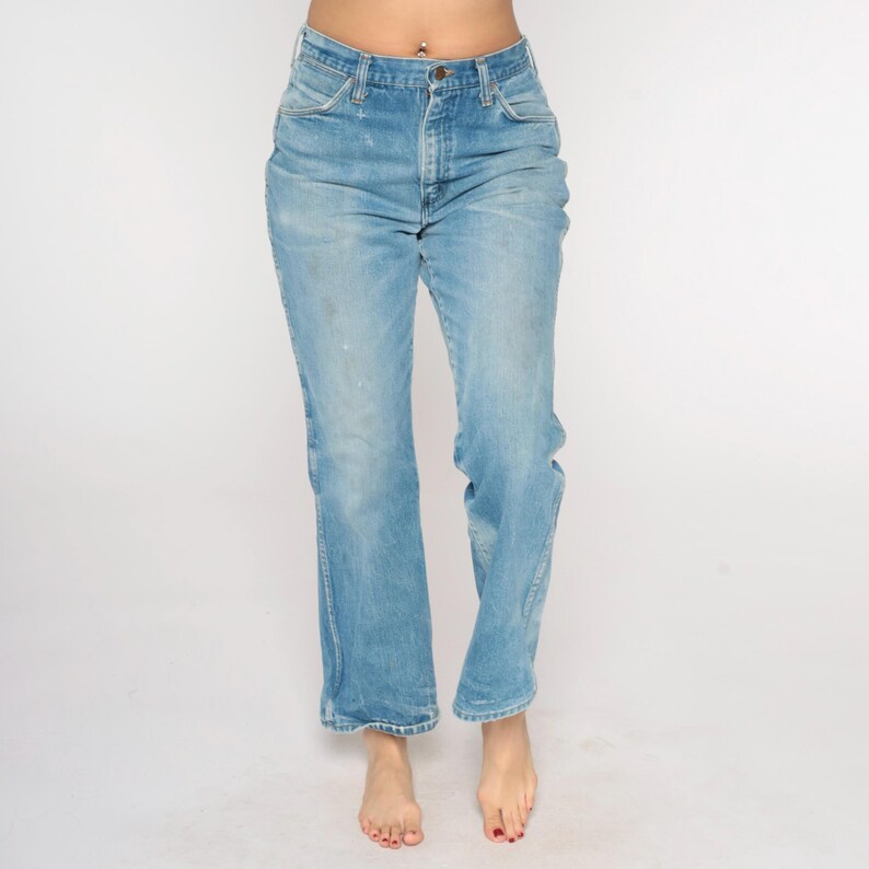 May include: Light blue denim jeans with a button and zip fastening. The jeans have a classic five-pocket design and a straight leg fit. The denim has a faded, worn appearance.