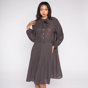 Könnte beinhalten: Ein dunkelgraues Kleid mit weißem Polka-Dot-Muster. Das Kleid hat lange Ärmel, eine Schleife am Ausschnitt und eine Knopfleiste vorne. Das Kleid reicht bis zur Mitte der Wade und hat einen ausgestellten Rock.