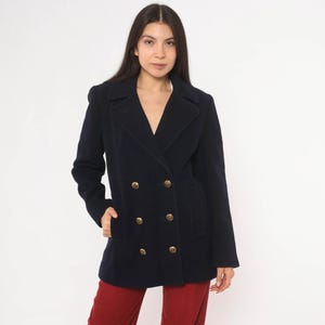 May include: A navy blue double-breasted pea coat featuring a wide notched lapel collar, long sleeves, and six gold-toned metallic buttons arranged in two vertical rows on the front. The coat has two side pockets and a structured, tailored fit.
