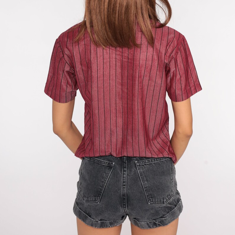 May include: A red and black striped short-sleeved shirt with a collared neckline. The shirt is worn with black denim shorts.