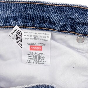 Peut inclure: Gros plan sur un jean en denim bleu avec un int&eacute;rieur blanc. Une &eacute;tiquette indique "Wrangler" avec la taille 32 x 34. Le jean est en 100% coton. L'&eacute;tiquette comprend &eacute;galement un code QR et d'autres d&eacute;tails.