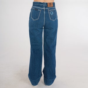 May include: A pair of high-waisted, wide-leg jeans in a dark blue wash. The jeans have a flower embroidered on the back pocket.