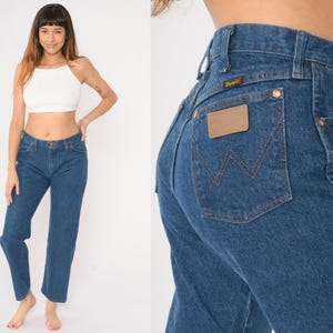 May include: A pair of blue denim jeans with a brown leather patch on the back pocket that says "Wrangler".
