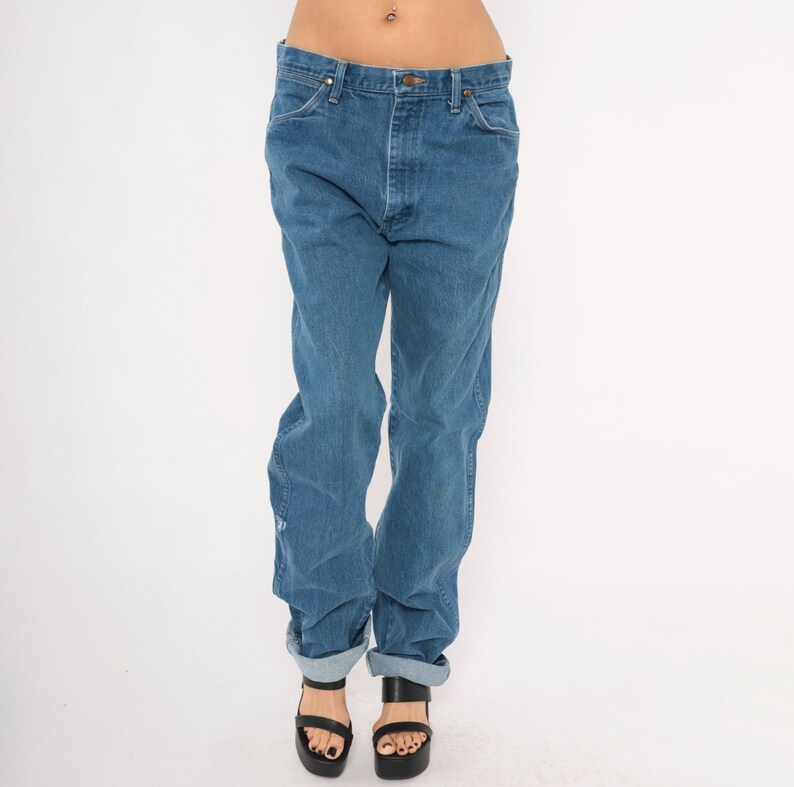 May include: Blue denim jeans with a classic fit, featuring a button and zipper closure, front and back pockets, and a straight leg. The jeans are cuffed at the ankles. The model is wearing black platform sandals.