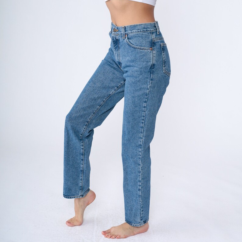 May include: Light blue denim jeans with a classic five-pocket design. The jeans have a straight leg cut and a medium wash. The model is wearing a white top. The jeans are made of a durable denim fabric.