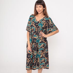May include: A knee-length dress with a V-neck and short sleeves. The dress features a black background with teal and gold scrollwork patterns. The model is wearing the dress in a studio setting with a white background.