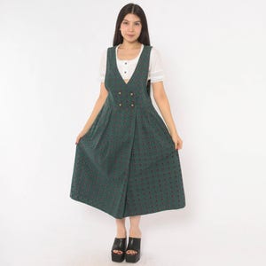 May include: A dark green sleeveless midi dress featuring a repeating circular pattern in a darker shade, a deep V-neckline, and a double-breasted front closure with four small buttons. The dress is layered over a white short-sleeved blouse.