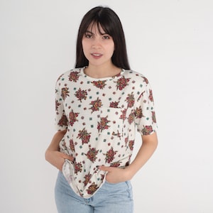 May include: A white short-sleeved shirt with a floral print. The shirt has a small pocket on the left side.