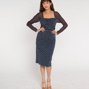 May include: A navy blue midi dress with white polka dots and a sheer black overlay. The dress has a square neckline and a fitted silhouette.