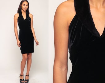 May include: A black velvet dress with a halter neckline and a knee-length hem. The dress features a faux fur trim around the neckline. The model is wearing black sandals.