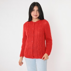 May include: A red cable knit cardigan with a button closure. The cardigan is made of a soft, fuzzy material.