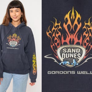 Puede incluir: Una sudadera con capucha azul marino con un gráfico de llamas y el texto "Sand Dunes Gordons Well".